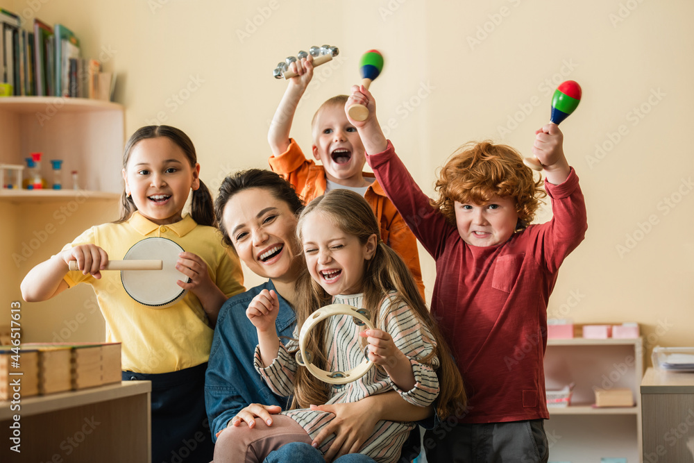 excited multiethnic kids playing musical instruments near happy teacher