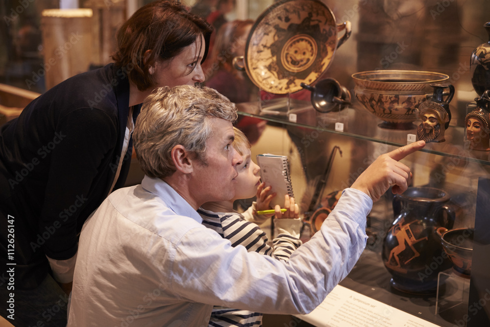 Family Looking At Artifacts In Glass Case On Trip To Museum