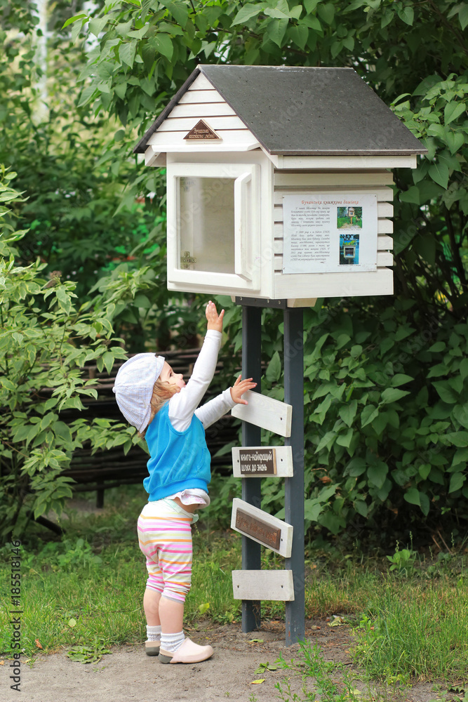 Little girl trying to get a book out of a community public street library. Book crossing.