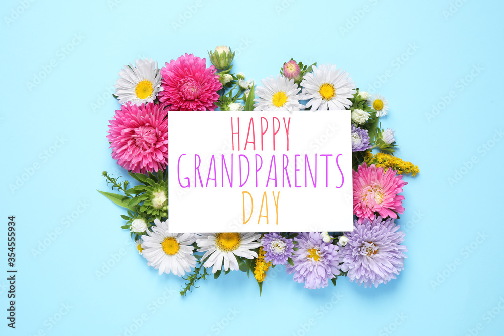 Flat lay composition with beautiful aster flowers and phrase HAPPY GRANDPARENTS DAY on light blue background