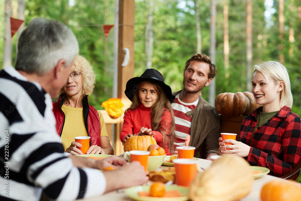 Family of five sitting by festive table on halloween day on terrace of their country house