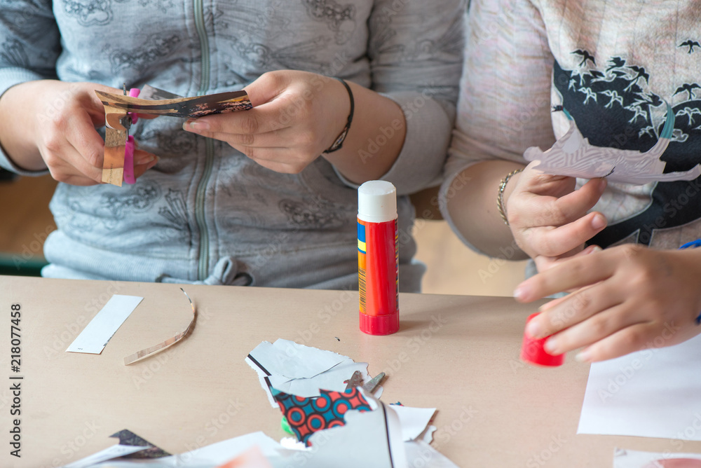 Creative workshop for kids. Little girls gluing cut out shapes and characters from magazines on white paper. Concept of art, crafts, kids having fun. Making collages and creating stories. Messy desk