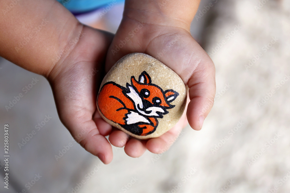 Young Child's Hands Holding a Painted Rock with A Cartoon Fox on It